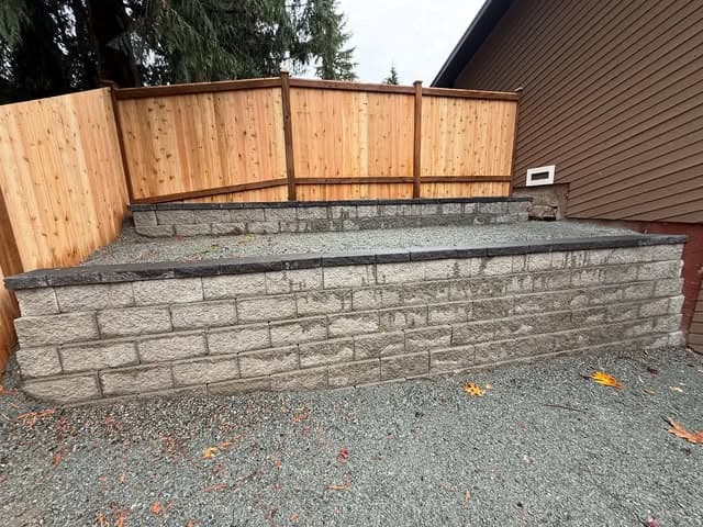 A grey segmental-block retaining wall topped by a new cedar fence.