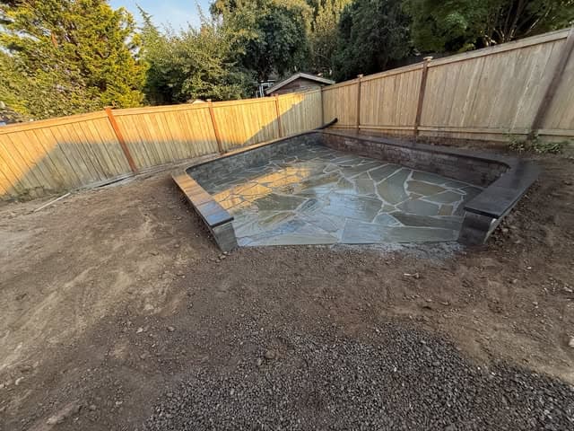 A flagstone patio set within a fresh stone border, taking shape against a new cedar fence.
