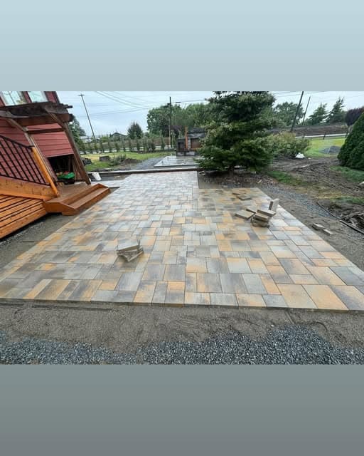 A newly laid multi-tone paver patio running out from a cedar deck toward an evergreen.